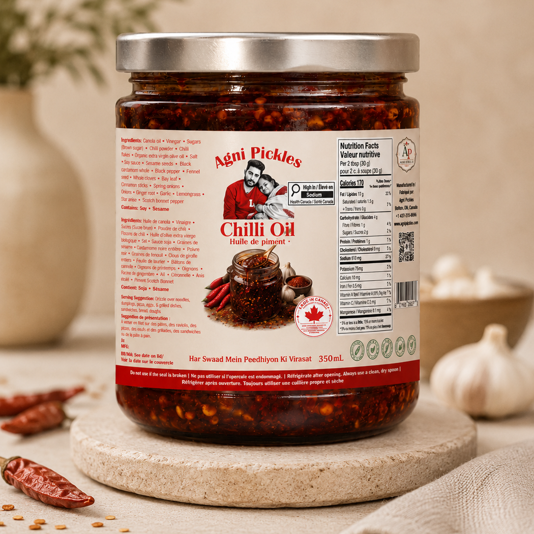 **Alt Image Description:** Jar of Agni Pickles Chilli Oil displayed with fresh chillies, garlic, spices, ingredients, nutritional facts, and the full product label in a rustic kitchen-style setting.