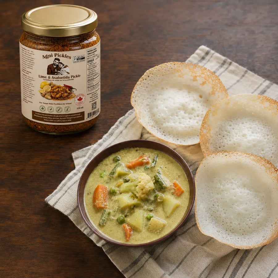 A jar of Mapi Pickles Lino & Anchoilla Pickle is shown next to a bowl of prepared pickle sauce with vegetables and three crispy round bread slices on a striped napkin over a wooden table.