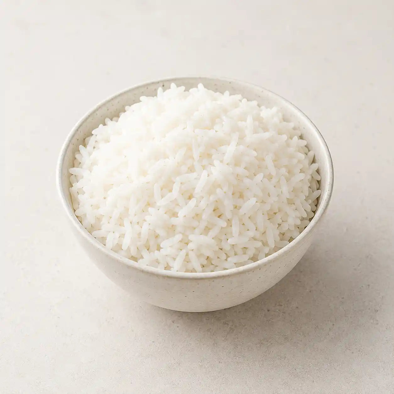 A small speckled off-white ceramic bowl filled with fluffy white rice, set against a neutral light beige background.