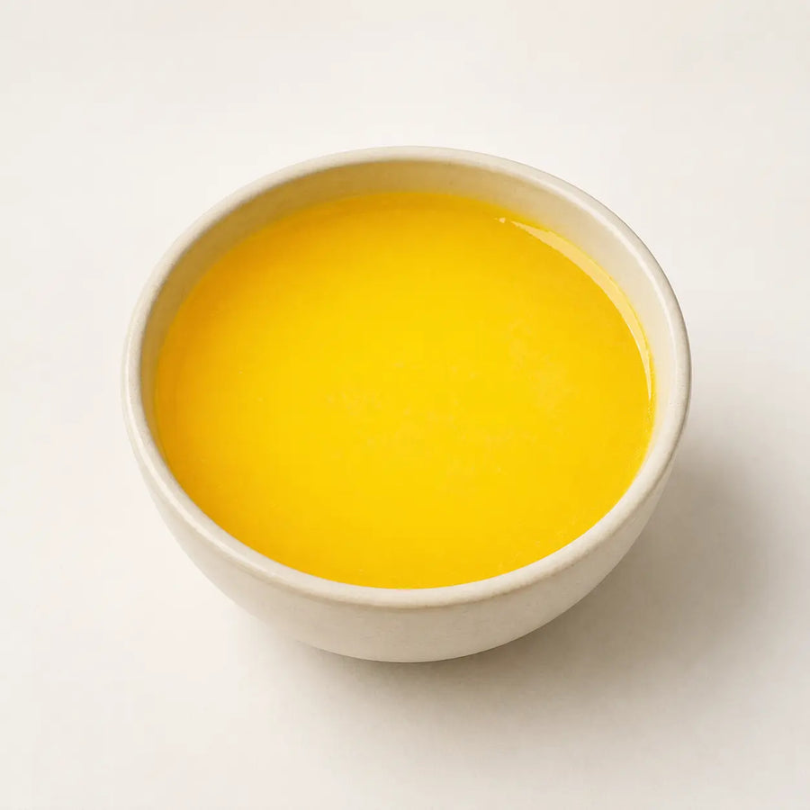 A small off-white ceramic bowl filled with bright yellow liquid, photographed from above on a clean white background.