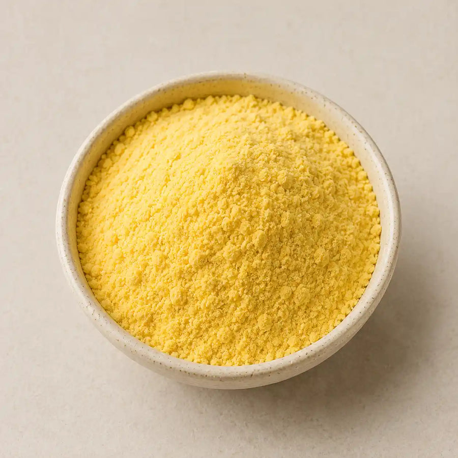 A small speckled ceramic bowl filled with bright yellow cornmeal powder, photographed from above on a light neutral background.
