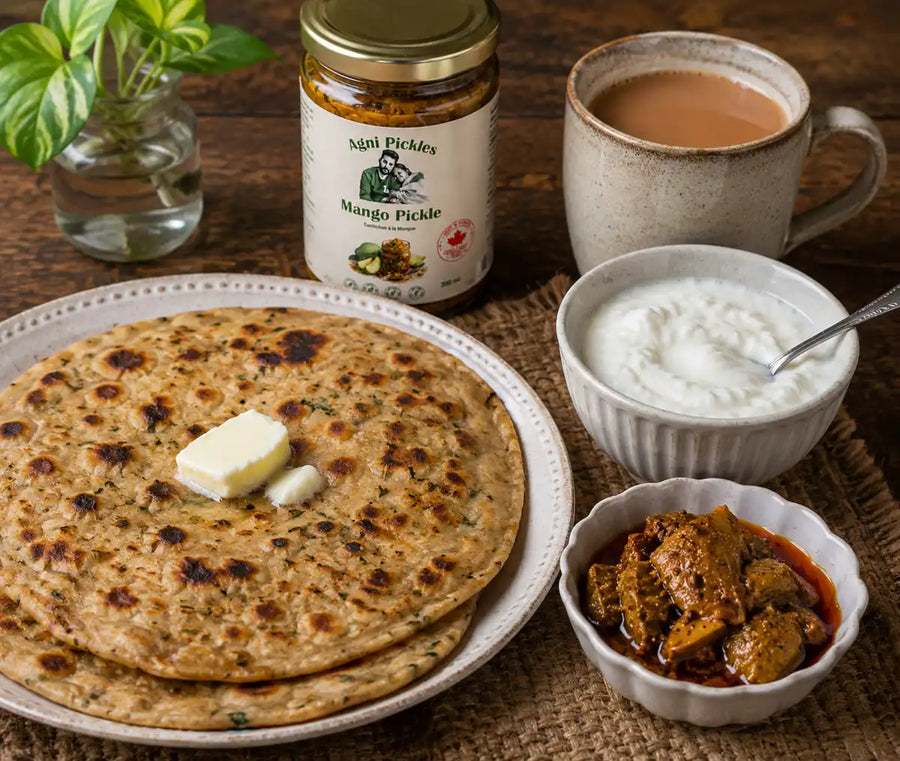 Rustic Indian breakfast with buttered parathas, homemade curd, chai, and Agni Pickles mango pickle on a wooden table.