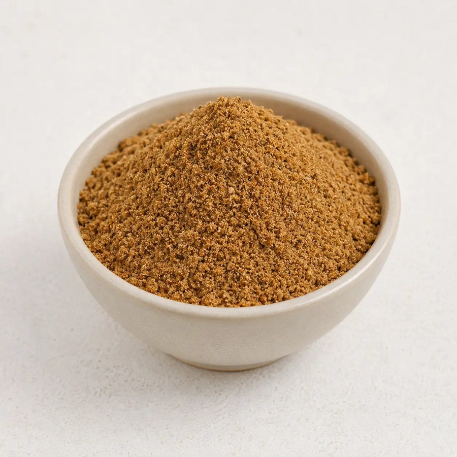 Chaat masala powder arranged in a small ceramic bowl on a clean light background.