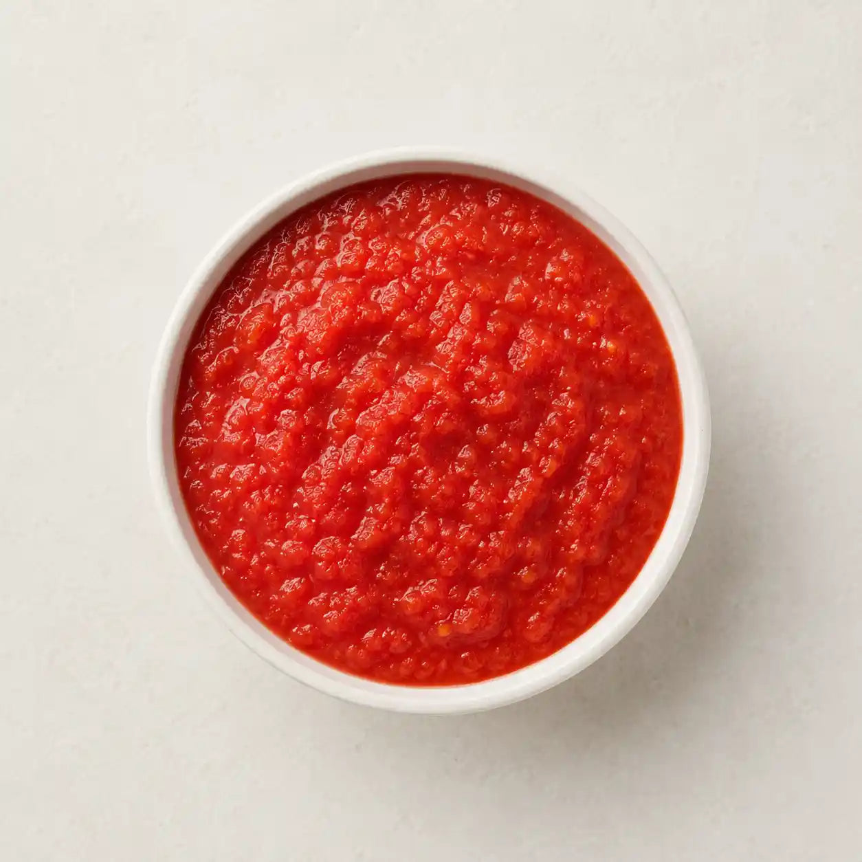 Crushed red tomatoes or tomato passata served in a small white bowl on a clean light background.