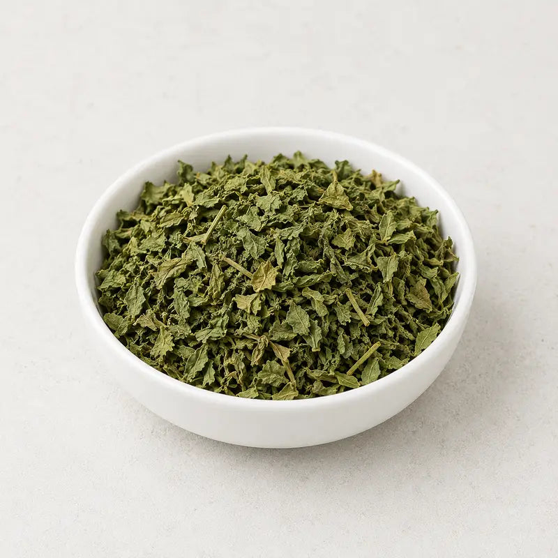 Dried kasuri methi leaves in a small white bowl on a light background.