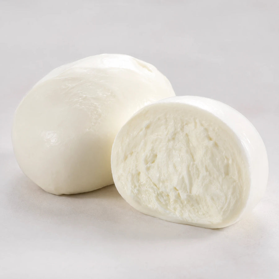 Two white mozzarella cheese balls, one whole and one sliced open to show the soft, creamy interior, photographed on a clean light gray background.