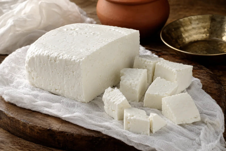 Fresh Indian homemade paneer block with hand-cut cubes resting on clean muslin cloth over a rustic wooden kitchen board.