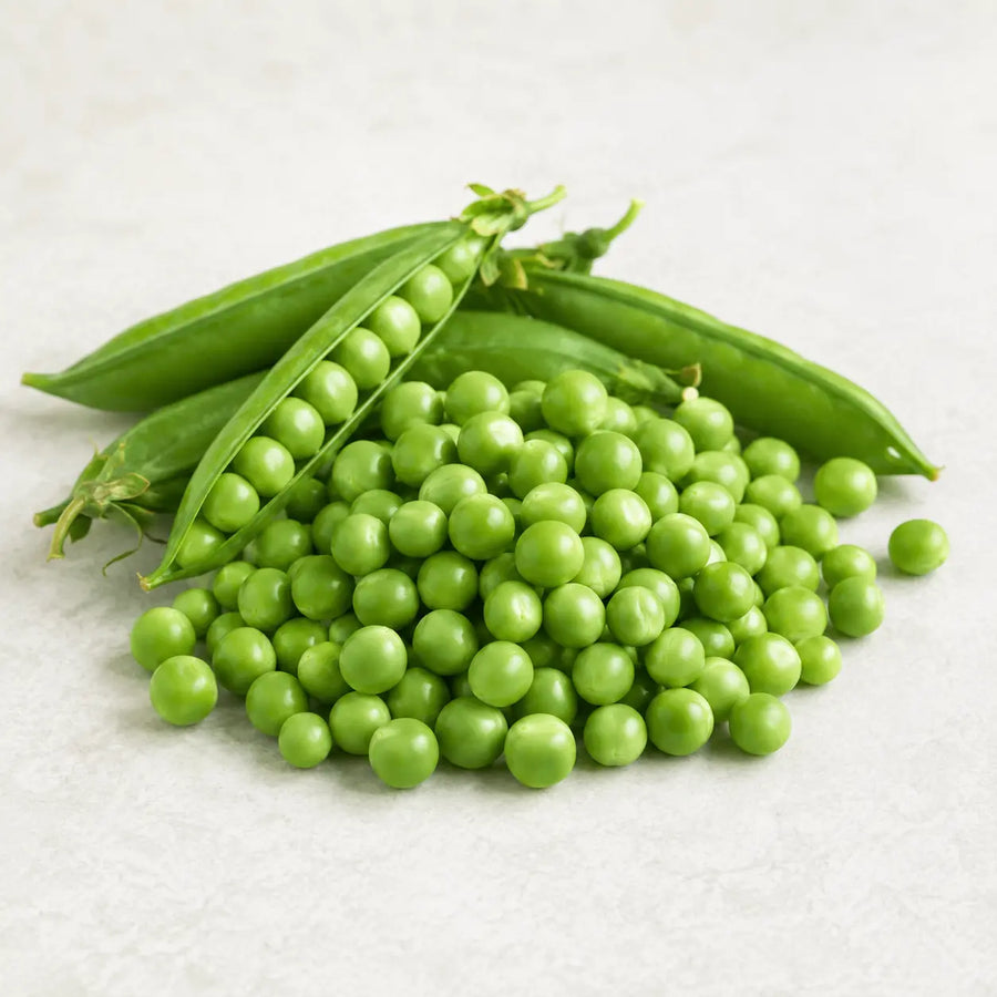Fresh green peas in pods and loose peas piled on a light off-white textured surface.