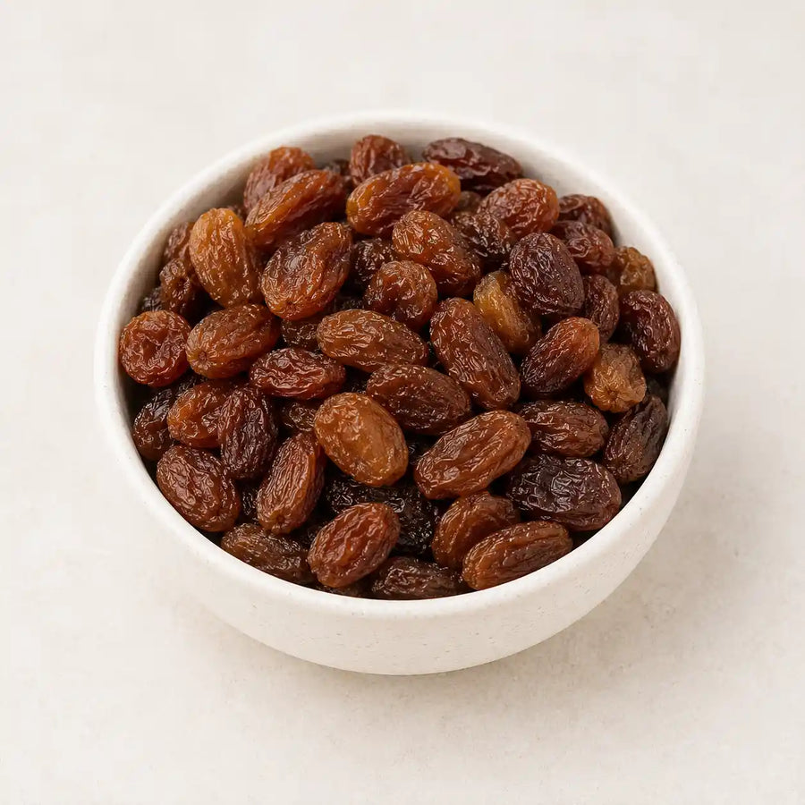 A white ceramic bowl filled with dried raisins on a light beige background.