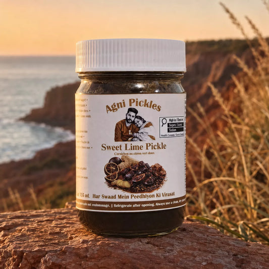 A jar of Agni Pickles Sweet Lime Pickle sits on a rocky cliffside with the ocean and dry grass in the background, during a warm sunset.