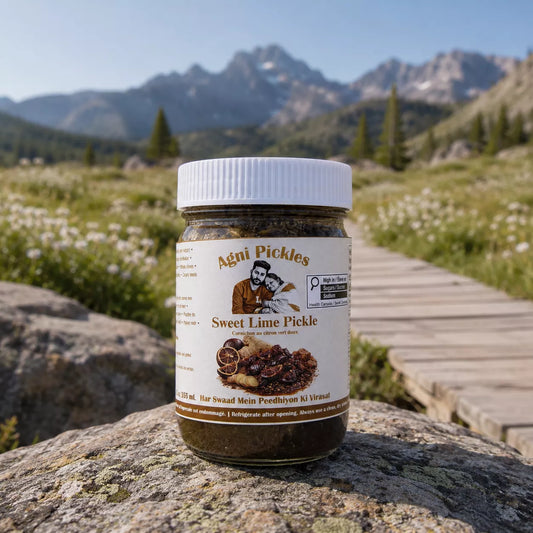 A jar of Agni Pickles Sweet Lime Pickle sits on a large rock in a mountain meadow, with a wooden boardwalk and mountains in the background.