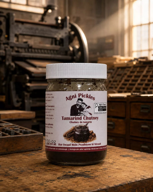 A jar of Agni Pickles Tamarind Chutney sits on a rustic wooden workbench in a vintage printing shop, with a warm, sunlit background.